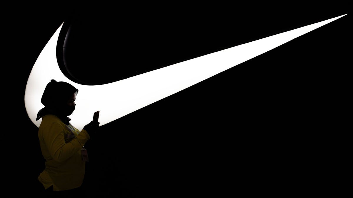 Frau steht vor einem großen, beleuchteten Nike Logo. Bild zum Nike Sale Artikel.