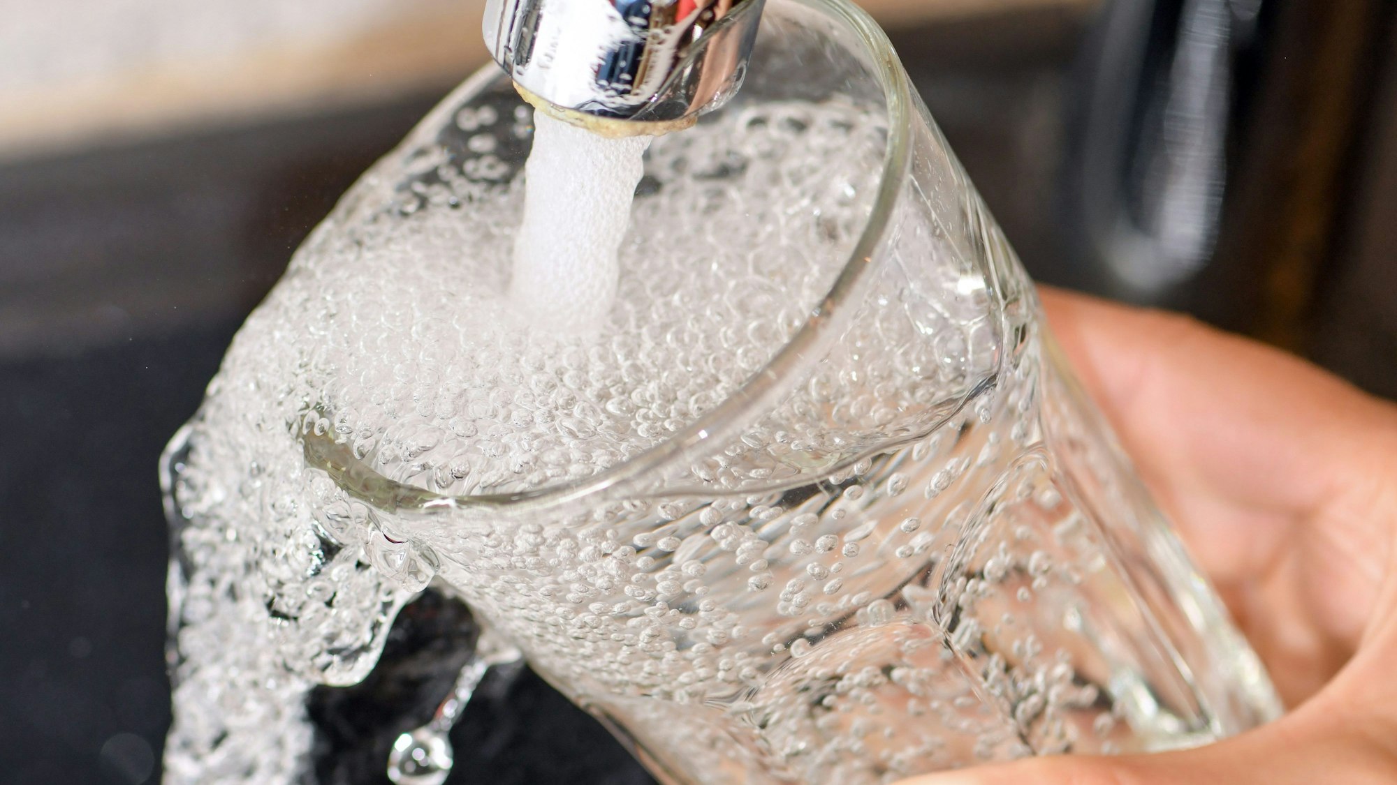 Am Wasserhahn in einer Küche wird ein Trinkglas mit Leitungswasser befüllt.