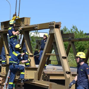 Acht THW-Helfer in blauer Arbeitskleidung und mit gelben Helmen arbeiten am Abbau einer massiven Stahlbrücke.