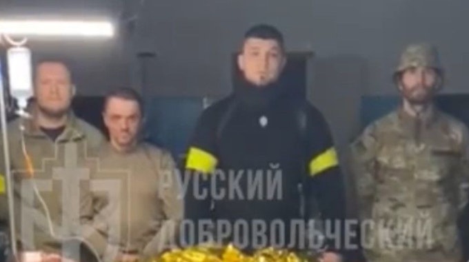 Kämpfer des „Russischen Freiwilligenkorps“ posieren in einem Video mit einem mutmaßlichen russischen Kriegsgefangenen. Der Anführer der Gruppe, schwarz gekleidet, ist der Neonazi Denis Kapustin, der mehrere Jahre in Köln gelebt hat.