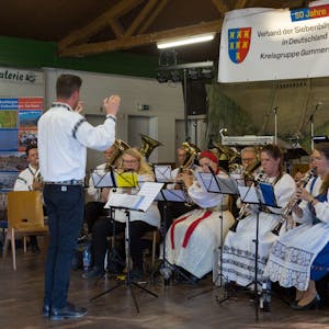 Ein Dirigent leitet ein Blasorchester, das in siebenbürgischer Tracht gekleidet ist.