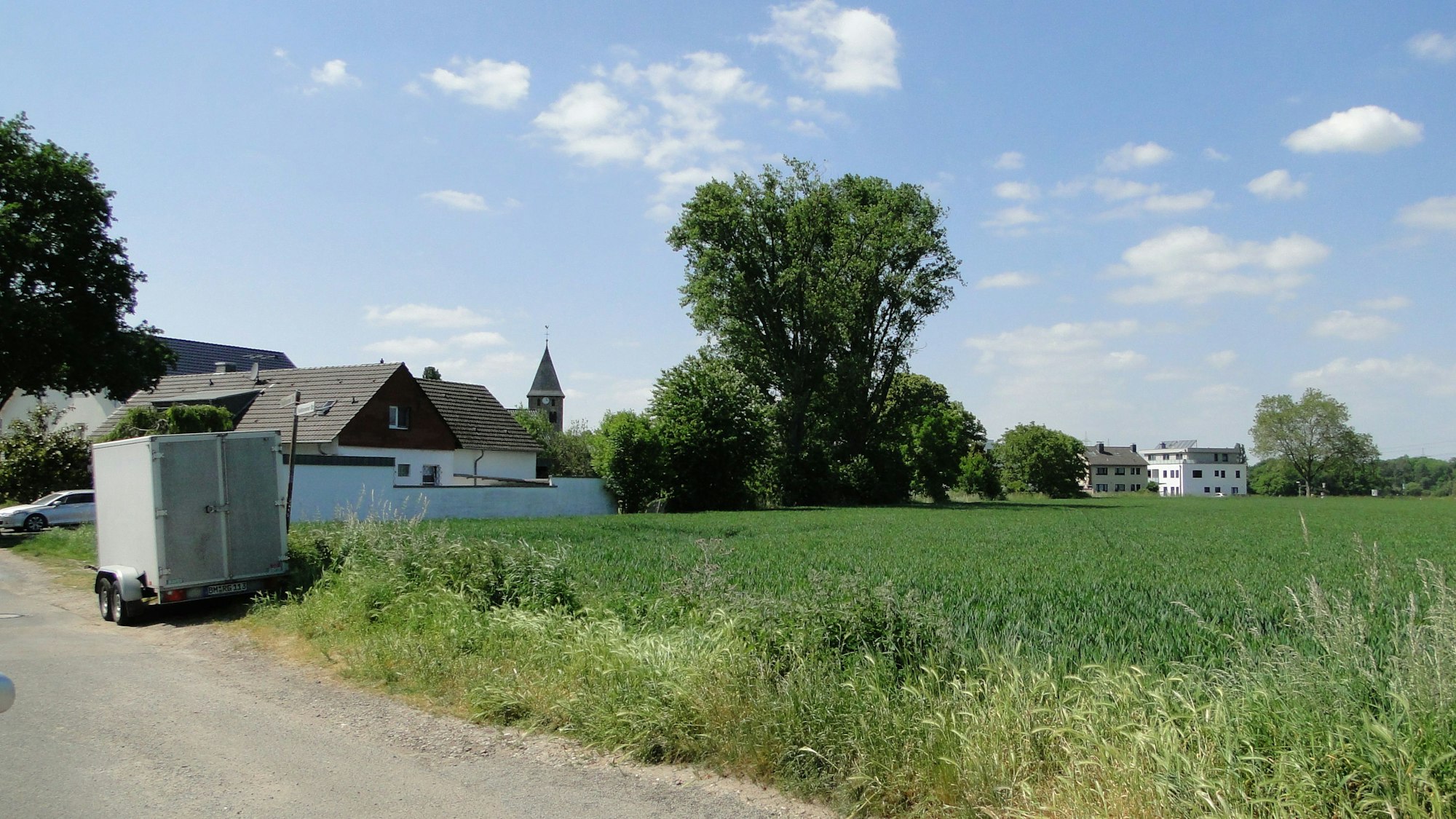 Das Feld zwischen Volkhovener Straße und Weilerstraße mit Häusern und Bäumen im Hintergrund.
