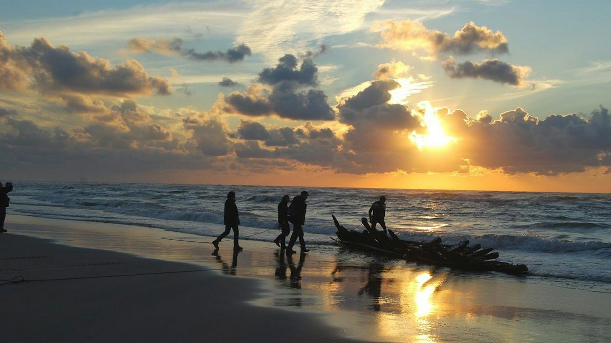 Menschen gehen im Sonnenuntergang am Strand entlang.
