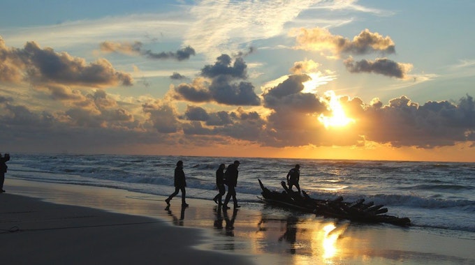 Menschen gehen im Sonnenuntergang am Strand entlang.