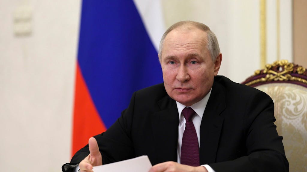 Wladimir Putin sitzt am Tisch und hält ein Dokument in der Hand.