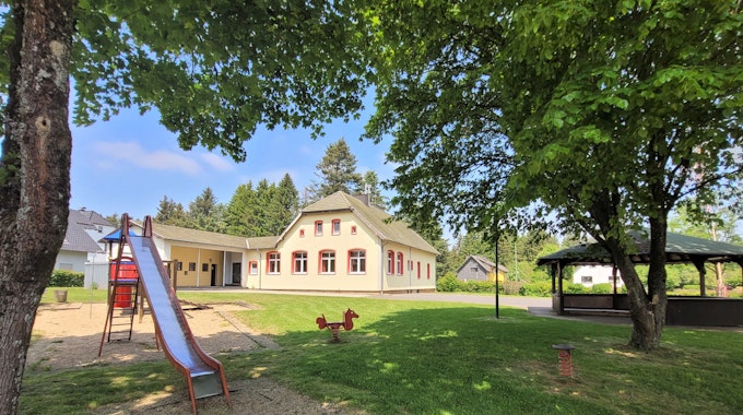 Das Bild zeigt den Dorfplatz in Broich mit einer Rutsche und einem Grillplatz. Im Hintergrund ist das Dorfgemeinschaftshaus zu sehen.