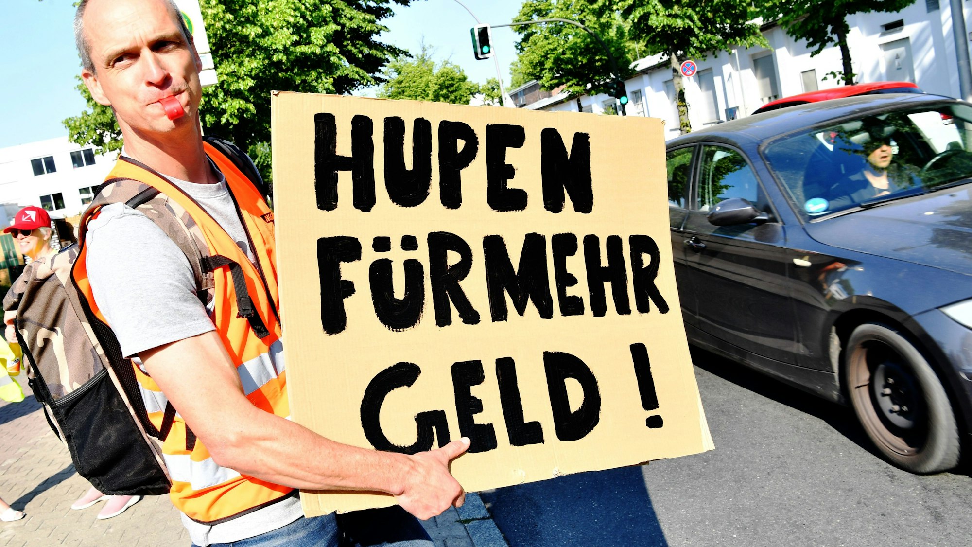 Ein Mitarbeiter einer Berliner Süßwarenfirma steht bei einem Warnstreik vor der Niederlassung von Bahlsen. Er hält ein Schild hoch mit der Aufschrift: „Hupen für mehr Geld!“