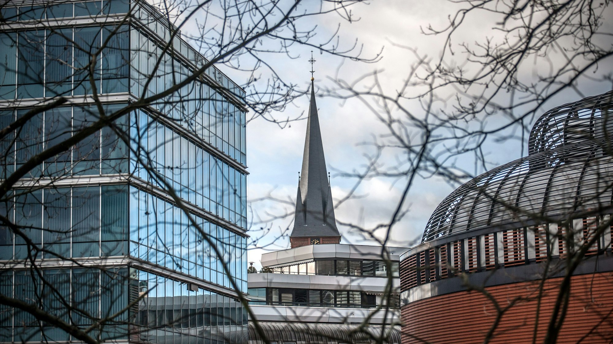 Turm der Christuskirche ragt zwischen Gebäuden in der Wiesdorfer City hervor.