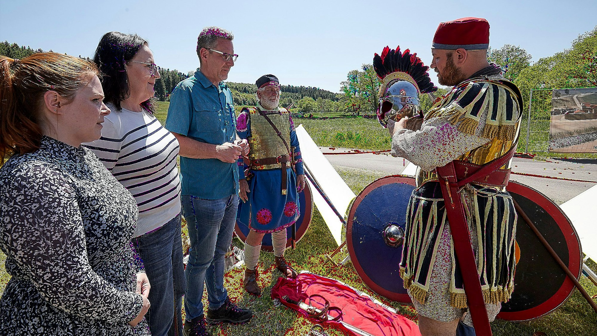 Ein Römer-Darsteller (r.) erklärt drei Besuchern seine Kleidung und den Helm.