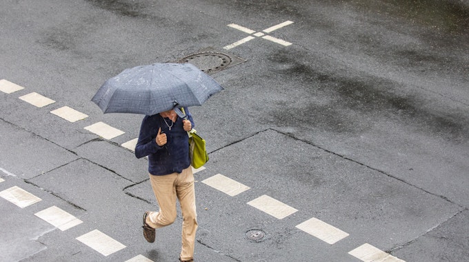 20.05.2022, Köln: Ein Mann geht mit einem Regenschirm in der Hand während eines Unwetters mit Gewitter und Starkregen im Ortsteil Sülz über die Straße. Foto: Matthias Heinekamp