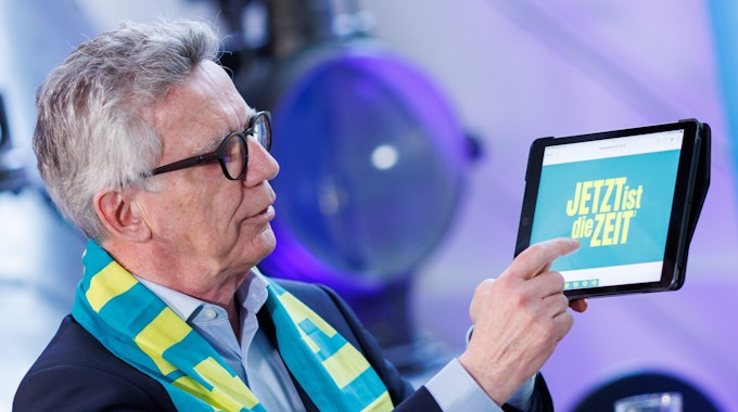 Thomas de Maizière (CDU), Präsident des 38. Deutschen Evangelischen Kirchentags in Nürnberg, präsentiert auf einem Tablet die Programm-App. Um den Hals trägt er einen Kirchentagsschal mit dem Motto „Jetzt ist die Zeit“.