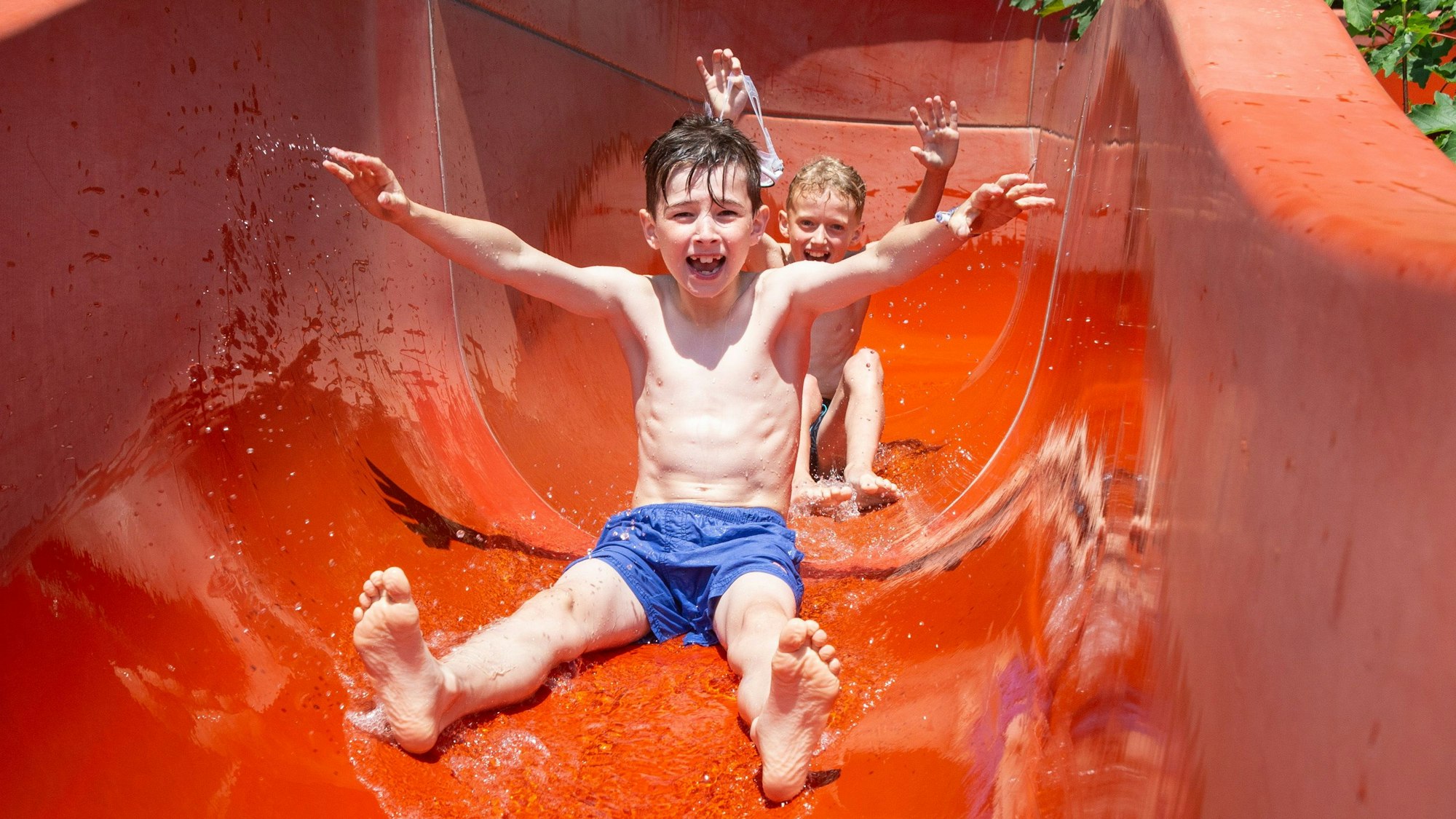 Zwei Kinder rutschen in einer roten Wasserrutsche in einem Freiband.