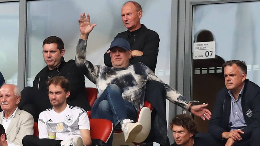 Nils Schmadtke (ober Reihe, links) sitzt neben seinem Vater Jörg Schmadtke, der inzwischen für den FC Liverpool arbeitet. Die beiden sind hier am 27. August 2022 in Leipzig zu sehen. Jörg Schmadtke macht Bewegungen mit den Armen.