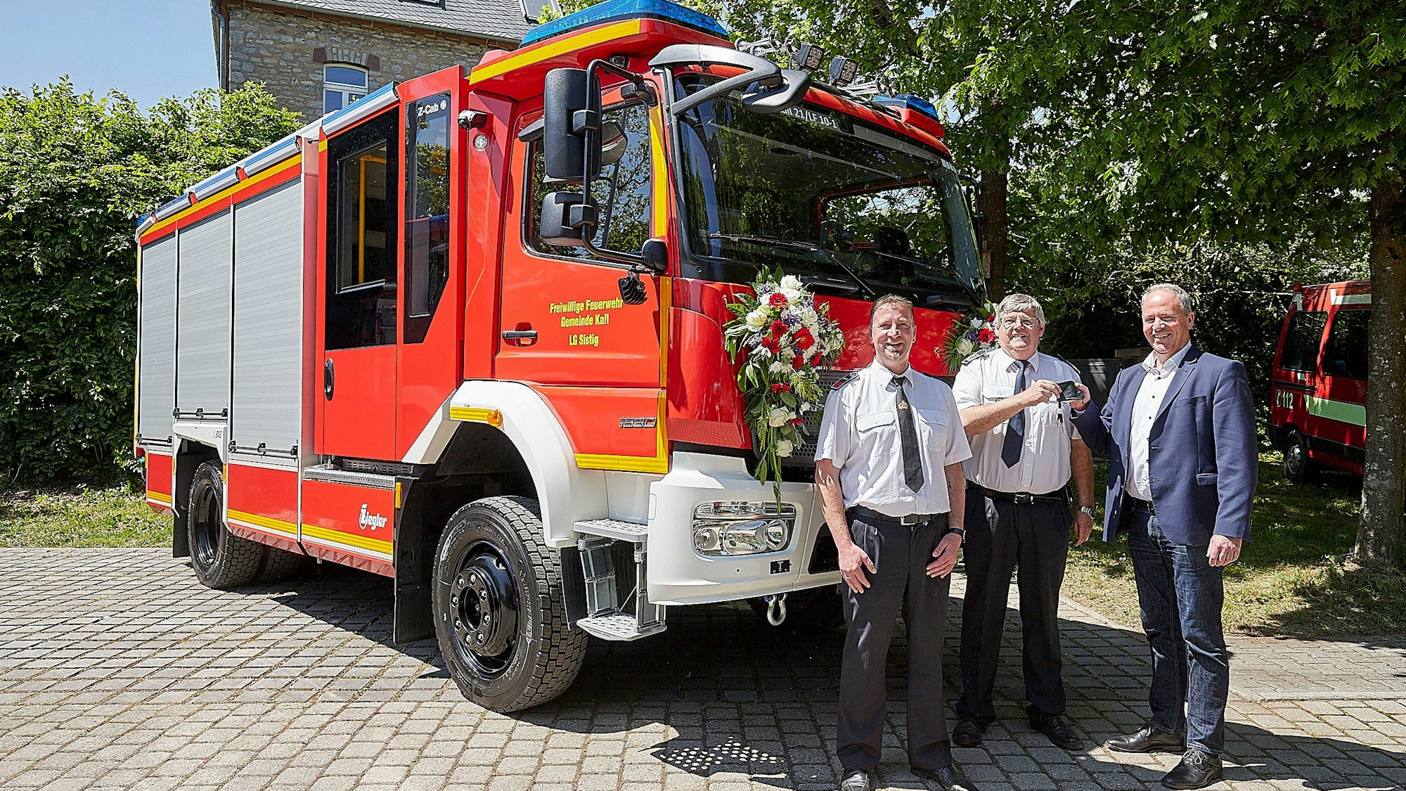 Löschgruppenführer Jochen Völler (v.l.), Kalls Feuerwehrchef Harald Heinen und Kalls Bürgermeister Hermann-Josef Esser stehen vor dem neuen Feuerwehrfahrzeug. Esser übergibt Heinen den Schlüssel.