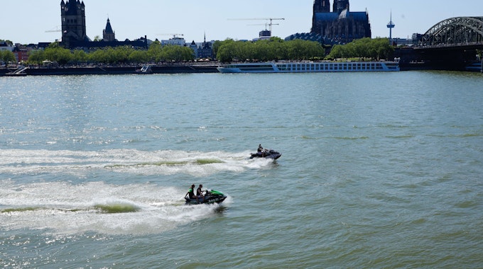 Jetski-Fahrer und Fahrerinnen sind auf dem Rhein unterwegs. Im Hintergrund sieht man den Kölner Dom.
