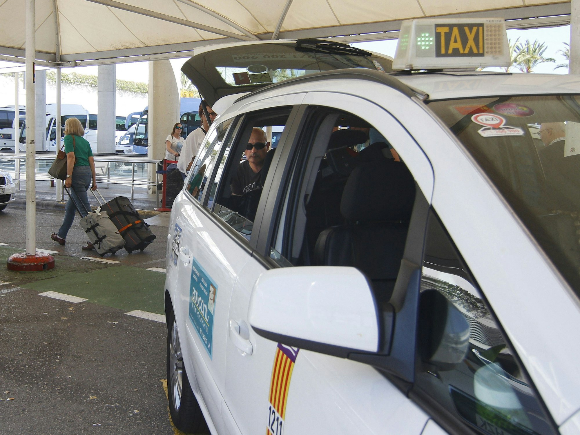 Ein Fahrer am Eingang des Flughafens von Palma de Mallorca. Er lädt einen Koffer in den Taxi-Kofferraum.