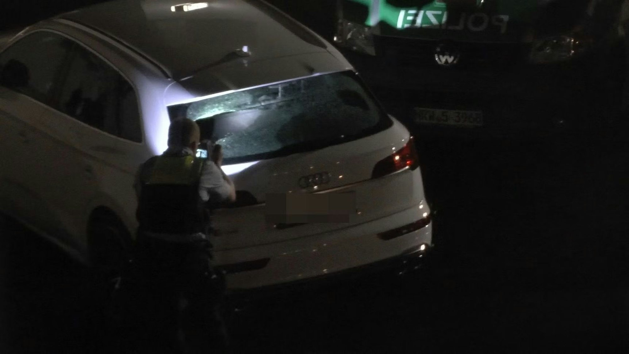 Ein weißes Fahrzeug wird von Polizisten untersucht.