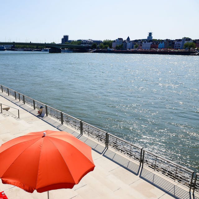 auf Treppen am Rhein steht ein roter Sonnenschirm