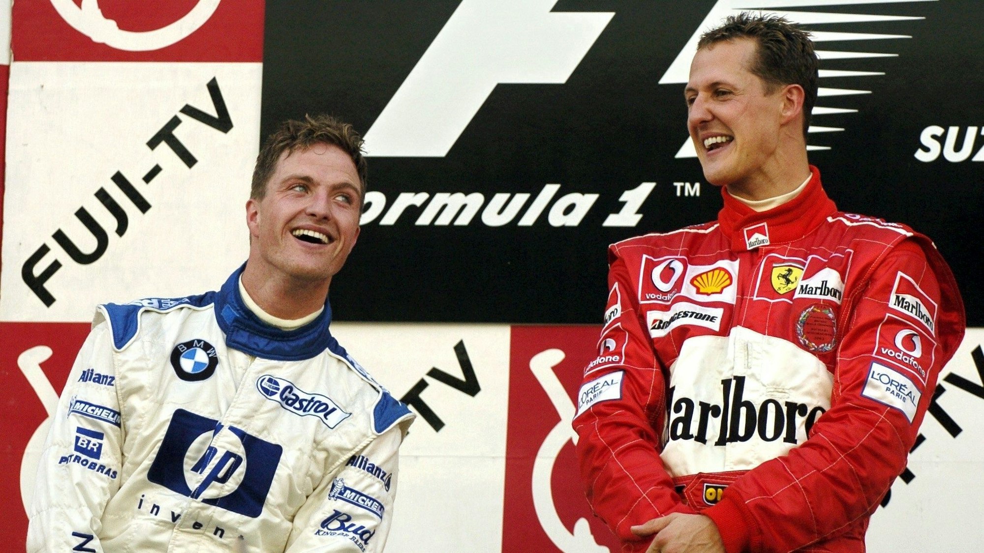 Die beiden ehemaligen Formel-1-Piloten Ralf (l.) und Michael Schumacher (r.) stehen gut gelaunt in Rennfahrermonturen auf dem Siegerpodest.
