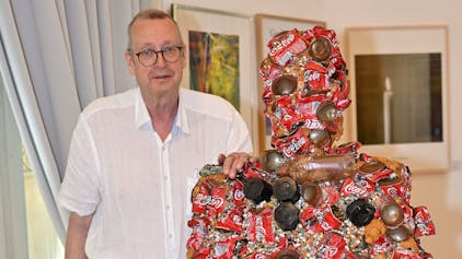 Dirk Kästel steht neben einem Kunstwerk, das HA Schult für die Ausstellung gespendet hat.