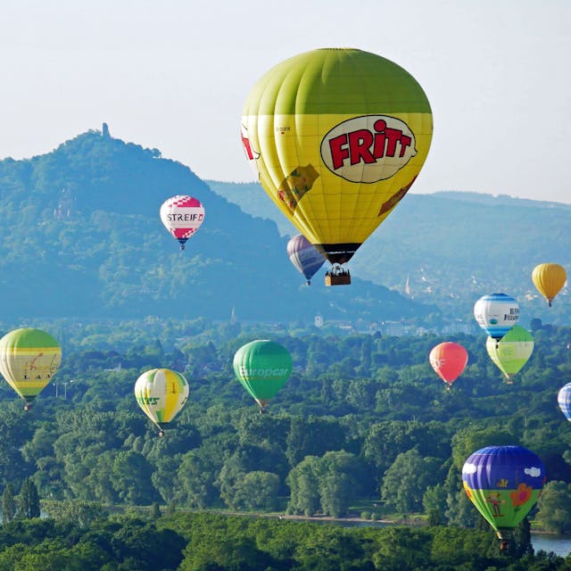 viele bunte Heißluftballone fahren über dem Rhein, Berge im Hintergrund
