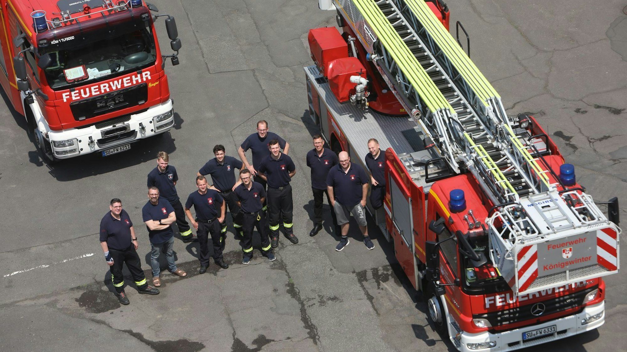 Elf Feuerwehrmänner stehen vor beziehungsweise neben Einsatzfahrzeugen, darunter die Drehleiter,
