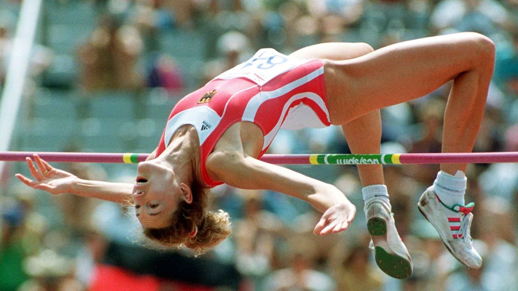 Die Hochspringerin Heike Henkel erreicht im Vorkampf bei den Olympischen Spielen in Barcelona die Qualifikationshöhe von 1,92 Meter. Man sieht sie bei einem Hochsprung in der Luft, direkt über der Latte.