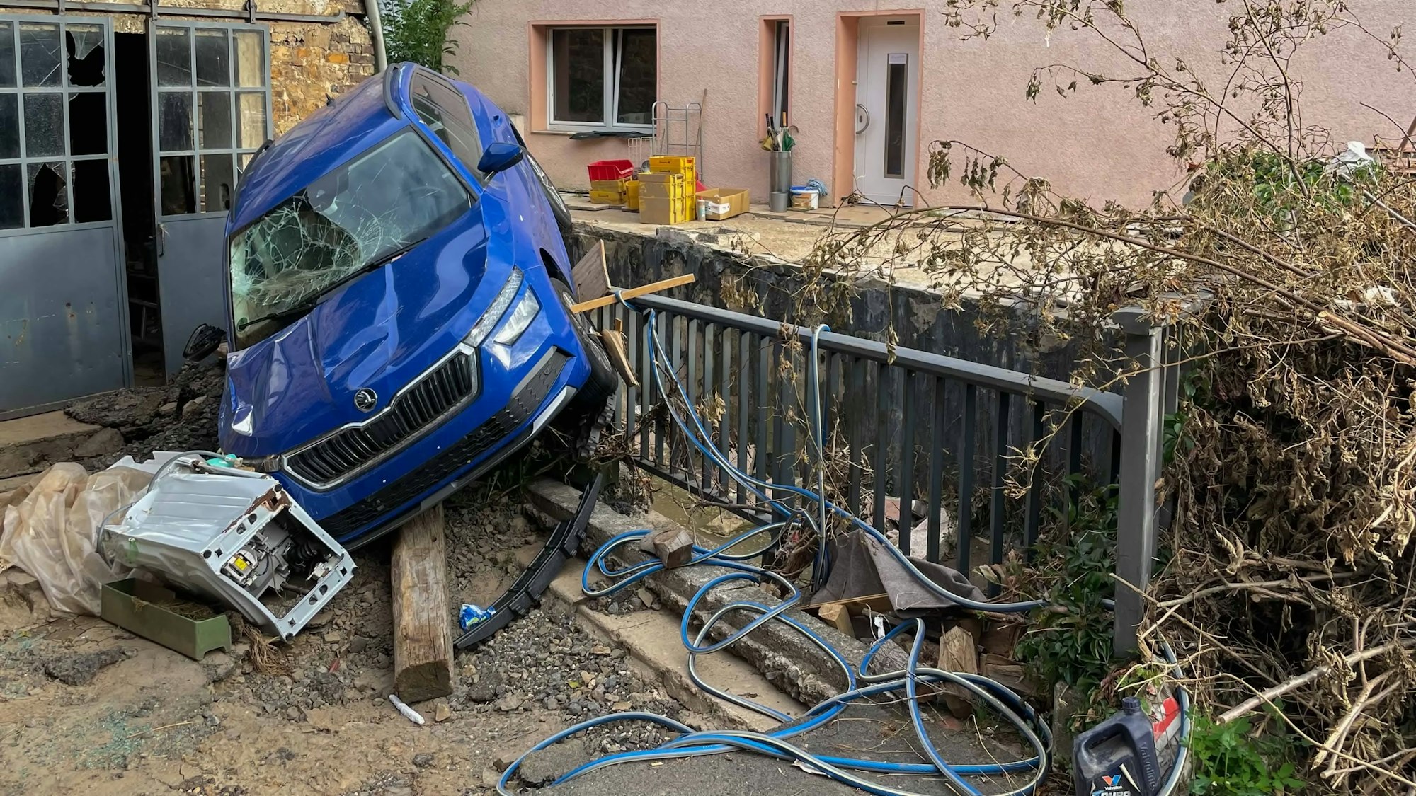 Das Bild zeigt die Zerstörung nach der Flut in Kreuzweingarten. Ein Auto ist auf ein Geländer gespült worden.