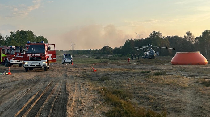Feuerwehrkräfte sind neben einem Löschhubschrauber in einem Waldstück nahe Jüterbog im Einsatz.