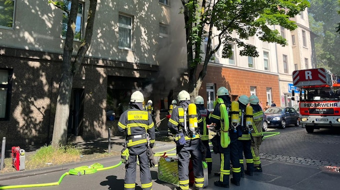 Feuerwehrleute stehen vor einem brennenden Bestattungsunternehmen in Köln-Humboldt.