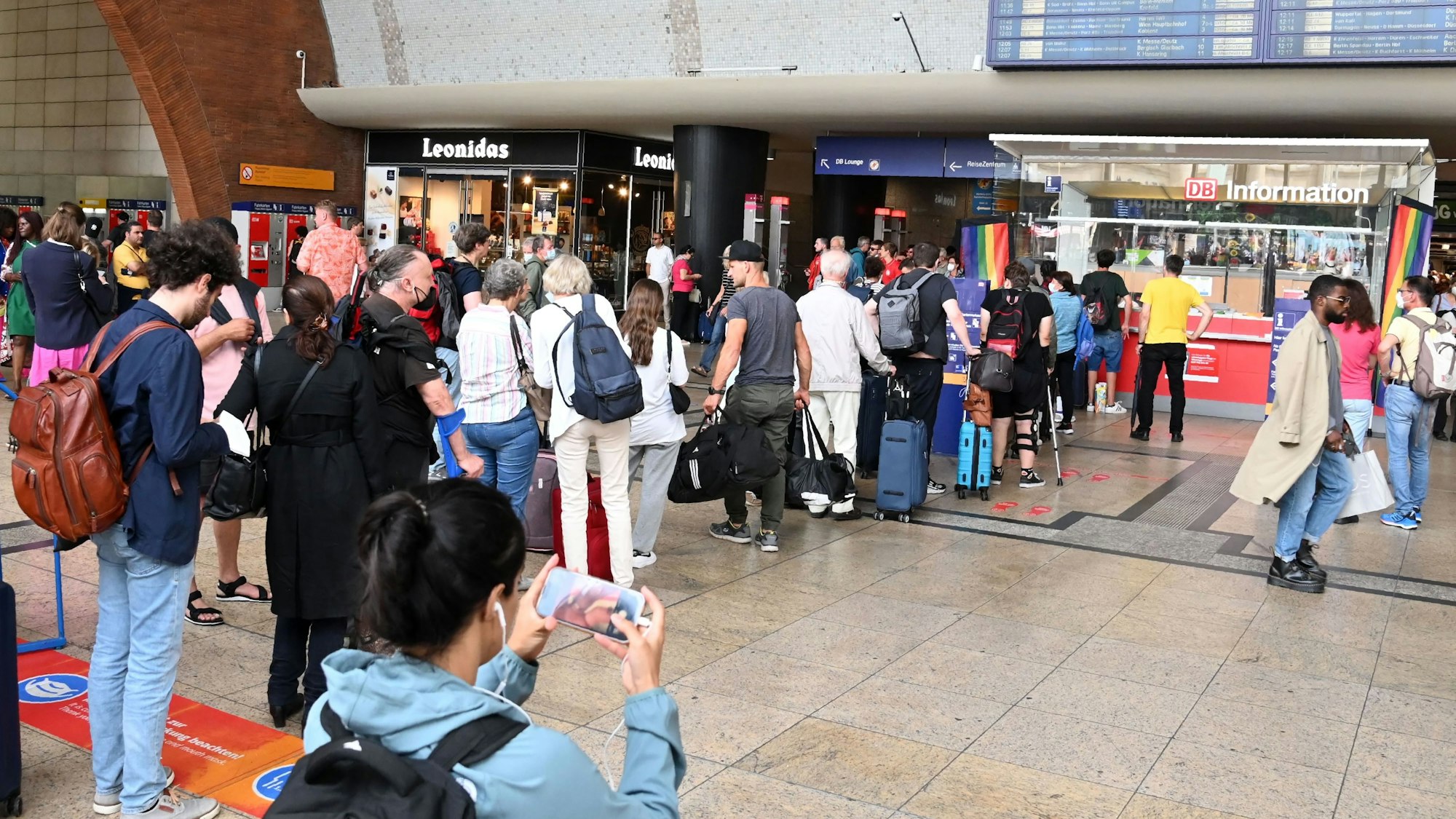 Menschen stehen am Hauptbahnhof in Köln am Infoschalter in einer Schlange.