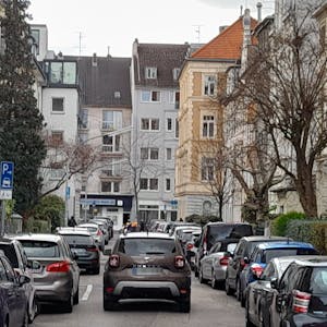 Ein Auto fährt durch eine schmale Straße, an der links und rechts Autos dicht an dicht parken.