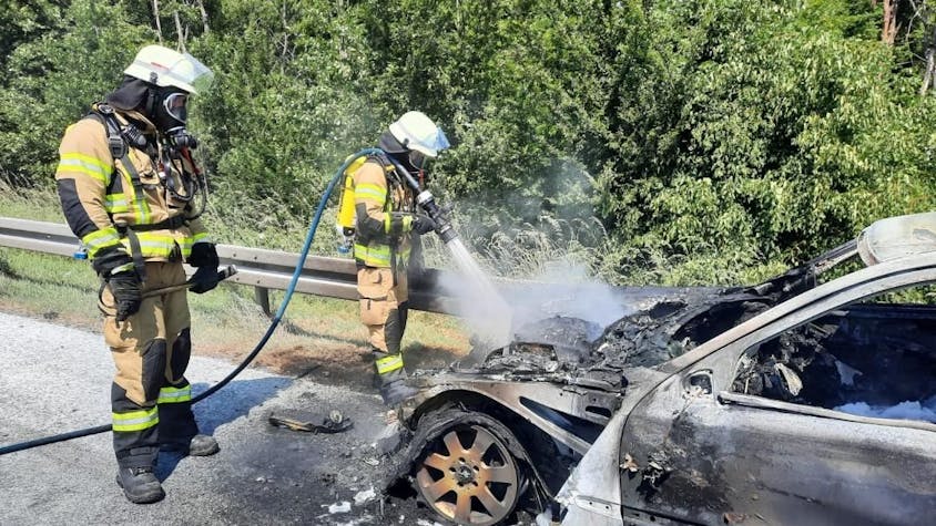Feuerwehrleute löschen ein brennendes Auto.