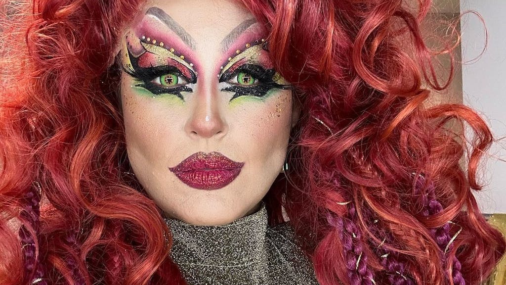 Moderatorin Nina Moghaddam als Drag-Queen mit buntem Make-up und roter Perücke bei der Show „Viva la Diva – Wer ist die Queen?“.