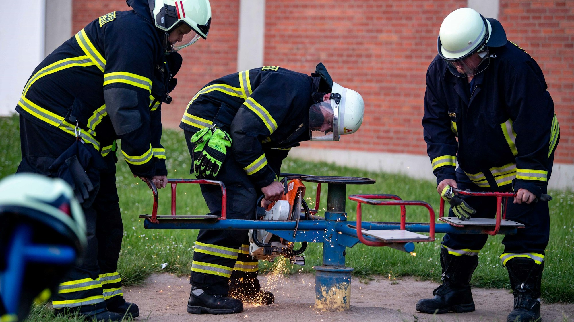 Drei Feuerwehrmänner trennen die Sitzfläche mit der Flex vom Spielgerät ab.