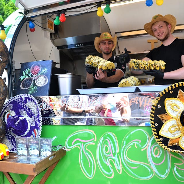 Zwei Männer mit Strohhüten stehen in einem Streetfood-Truck.