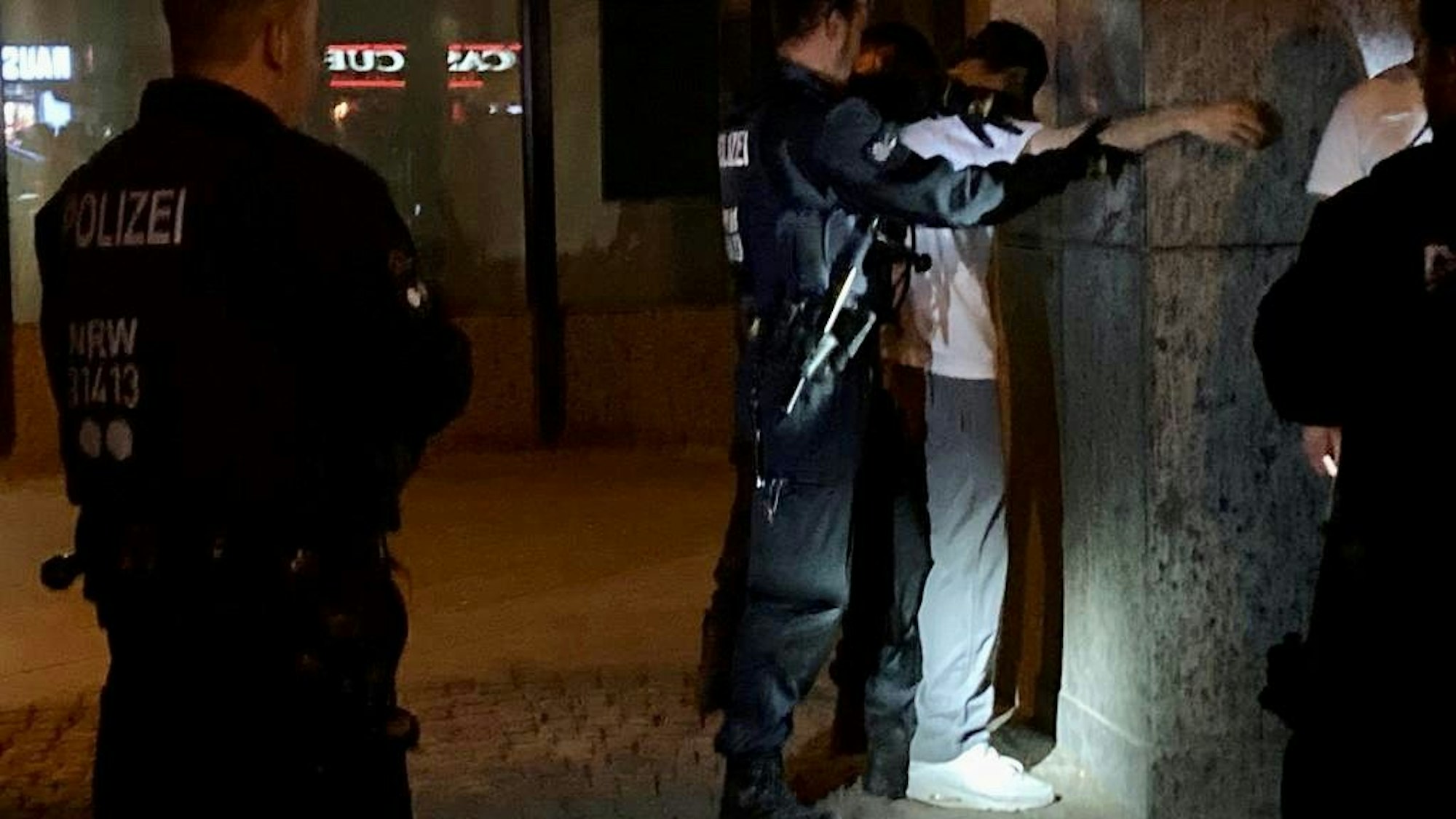Ein Mann steht an einer Wand und wird von Polizeikräften abgetastet.