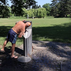 Ein Mann trinkt im Park aus einem Trinkwasserspender.