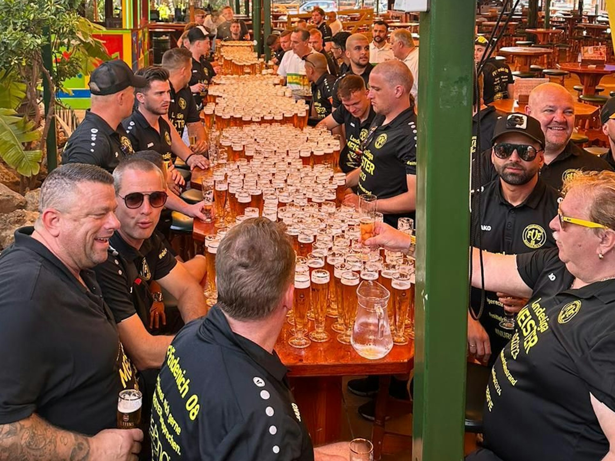 Spieler und Betreuer des FV Bonn-Endenich sitzten an einer langen Tafel, auf der unzählige volle Biergläser stehen.