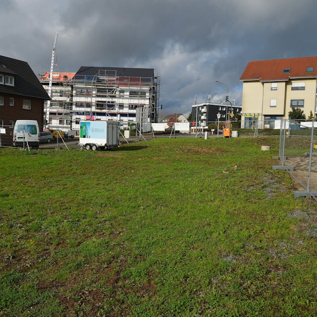 Rechts am Bildrand sind die Absperrgitter um eine grüne Wiese zu sehen. Im Hintergrund sowie am linken Bildrand sind Wohnhäuser zu sehen.