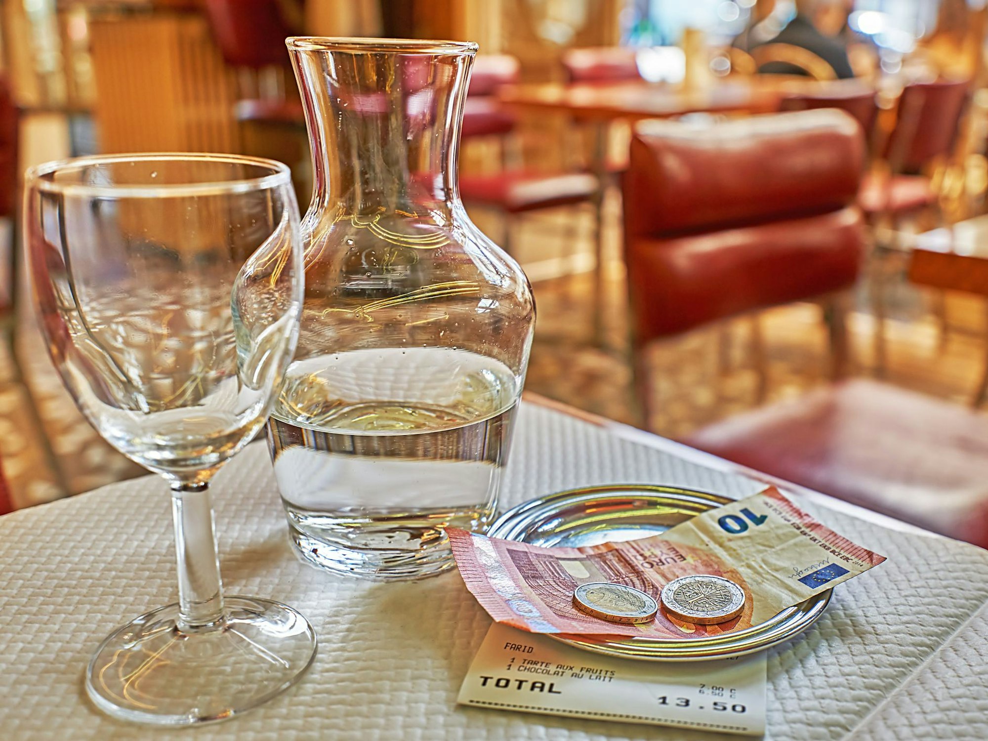 Man sieht Trinkgeld auf einem kleinen Teller auf dem Tisch liegen, neben einer Glaskaraffe und einem Trinkglas.