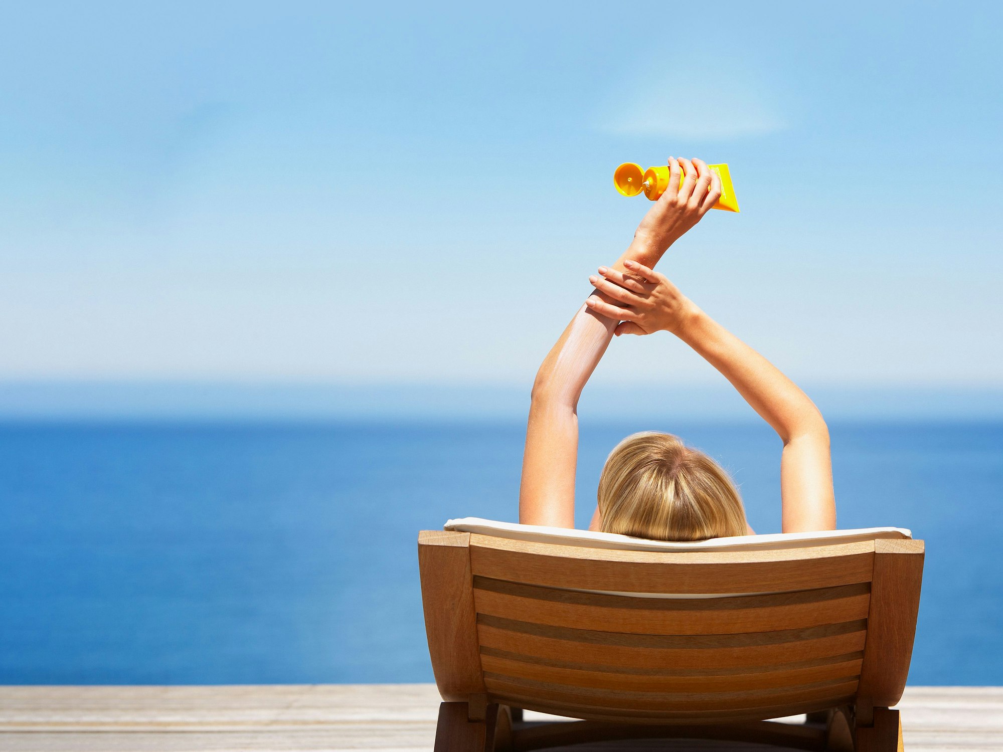 Relaxte Frau am Strand mit Sonnencreme-Tube in der Hand