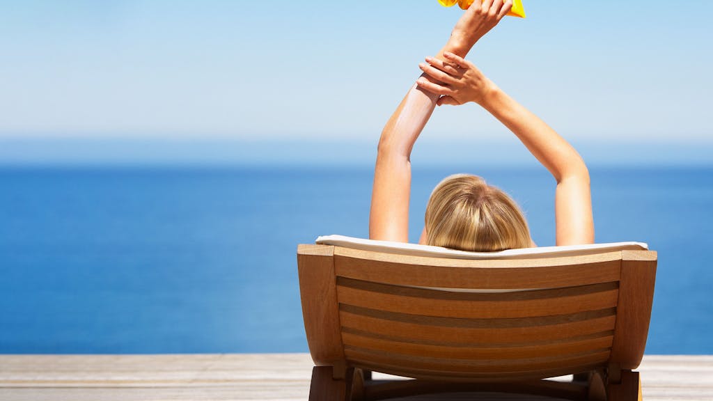 Relaxte Frau am Strand mit Sonnencreme-Tube in der Hand