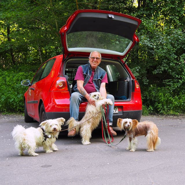 Karl-Heinz Schneider sitzt im Kofferraum seines Autos mit drei Hunden an der Leine.