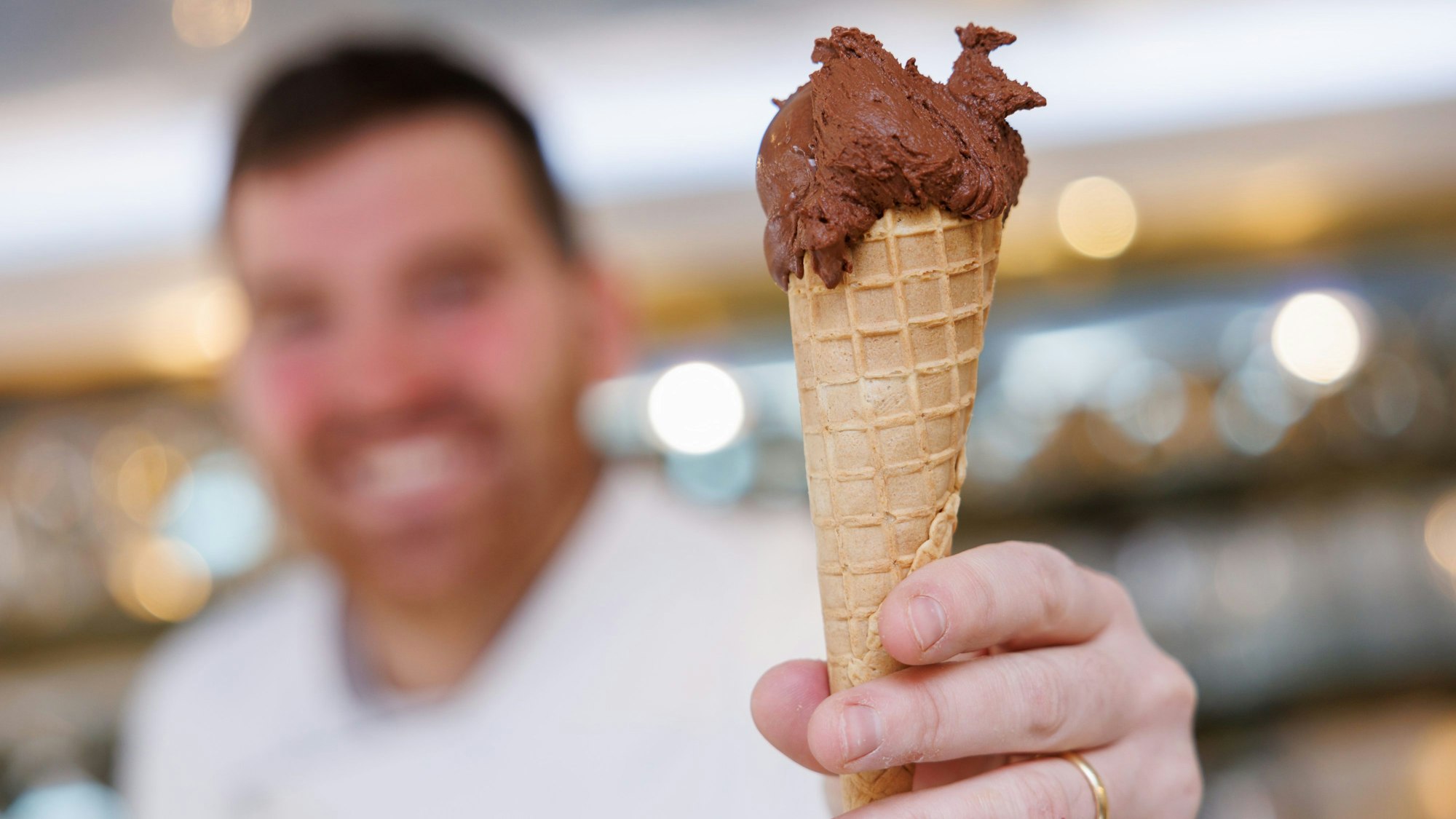 Der Eismacher Luca de Rocco hält in seinem Eiscafé eine Waffeltüte mit einer Kugel veganem Schokoladeneis in der Hand.