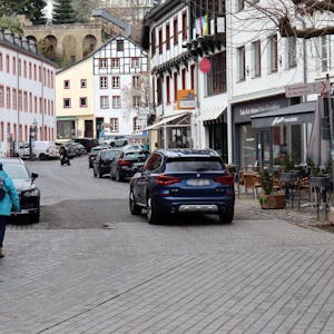 Blick in die Marktstraße in Bad Münstereifel, auf der ein Auto und Fußgänger unterwegs sind. Am Straßenrand parken weitere Autos.