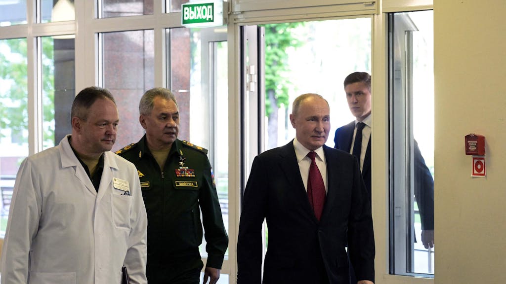 Russlands Präsident Wladimir Putin und sein Verteidigungsminister Sergei Schoigu treten zusammen mit einem Arzt durch die Tür eines Krankenhauses.