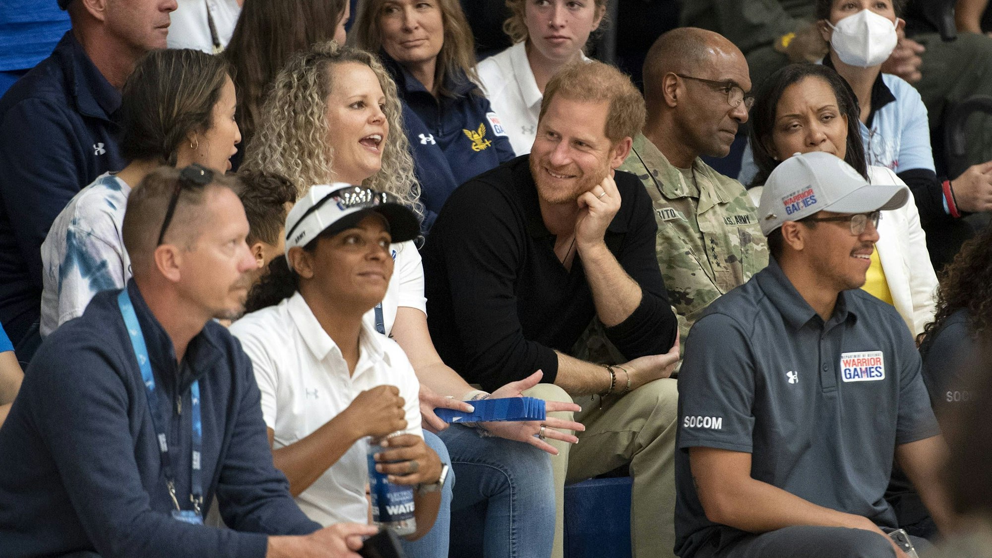 Prinz Harry sitzt bei einem Volleyballspiel bei den 2023 Warrior Games im Publikum und unterhält sich mit Anwesenden.