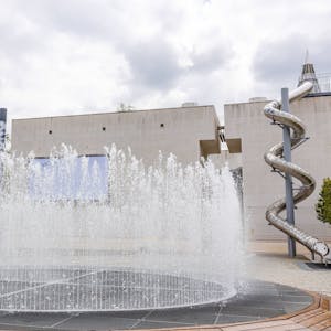 Ein Springbrunnen spritzt Wasser vor der Bundeskunsthalle. Am Rand stehen 16 Säulen, die die Bundesländer symbolisieren.&nbsp;