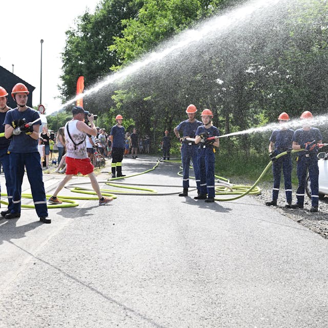 Mehrere junge Feuerwehrleute schießen Wasser aus zwei Schläuchen.